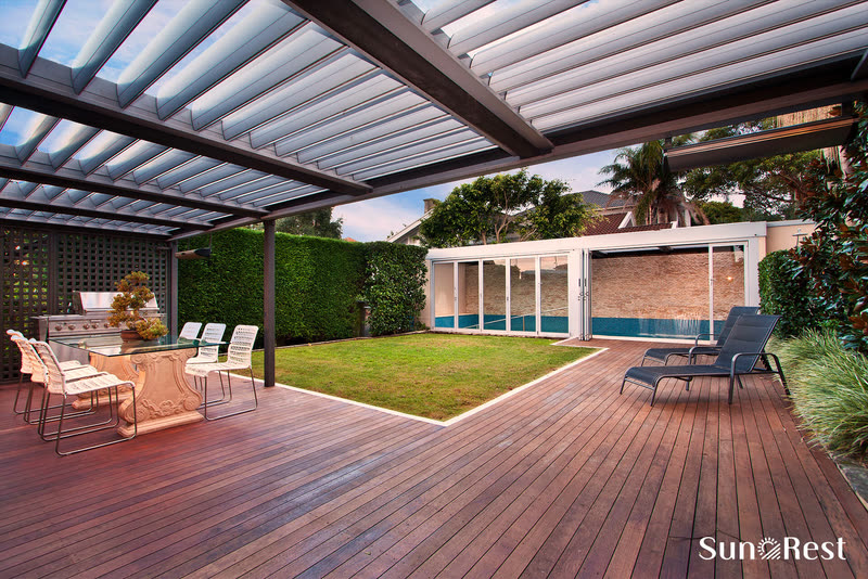 Pergola SunRest nad drewnianym tarasem z leżakami, grillem i strefą jadalną
